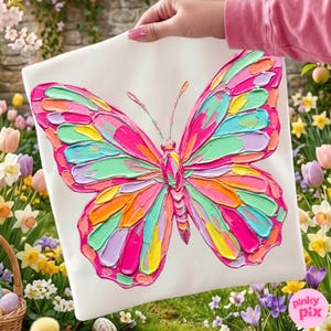 May include: A white square canvas featuring a vibrant, textured butterfly painting. The butterfly's wings are a mosaic of bright colors including pink, green, yellow, and orange. The artwork is held up by a person, with a background of flowers.