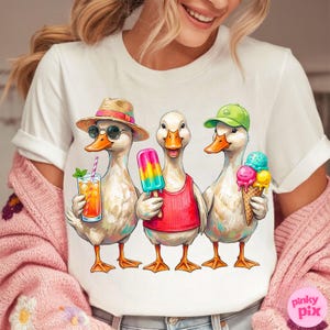 May include: White t-shirt featuring a whimsical illustration of three ducks enjoying summer treats. One duck wears a straw hat and sunglasses, holding a drink. Another has a popsicle, and the third holds an ice cream cone. The ducks are wearing a red tank top and a green cap.