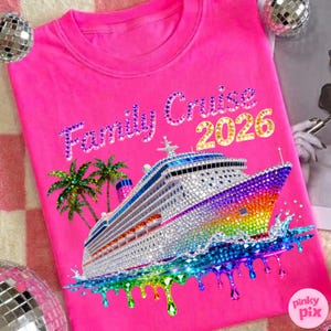 Op de afbeelding: Een felroze t-shirt met de tekst "Family Cruise 2026" in sprankelende letters. Een met juwelen bezet cruiseschip met regenboogaccenten en palmbomen staat op de voorkant. Het ontwerp bevat druppelend regenboogwater.