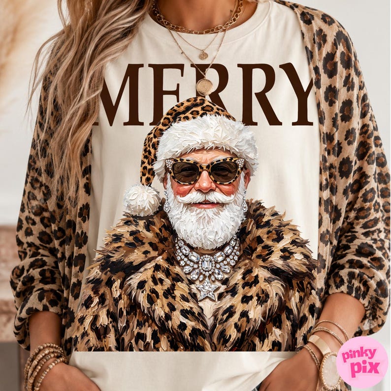 以下が含まれることがあります： クリーム色のTシャツ。茶色の文字で「MERRY」と書かれ、その下にヒョウ柄のサングラスと帽子を身につけ、ヒョウ柄のフェイクファーコートの上に大きなクリスタルのステートメントネックレスをつけたサンタクロースのグラフィックがプリントされています。