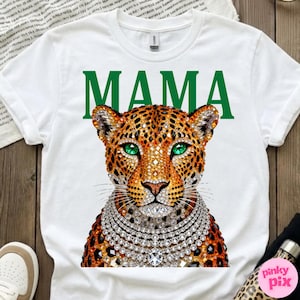 May include: White t-shirt with a leopard design, green eyes, and a diamond necklace. The word "MAMA" is printed in green above the leopard's head. The leopard has a brown and orange spotted coat.