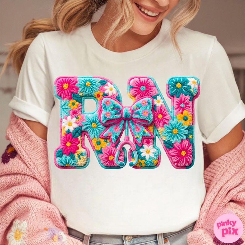 May include: White t-shirt with a colorful floral design spelling "RN". The letters are filled with pink, blue, yellow, and white flowers. A blue bow and stethoscope are in the center. The shirt is a nurse-themed design.
