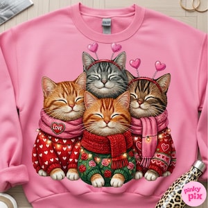 May include: Pink crewneck sweatshirt featuring a graphic of four smiling cats. The cats wear scarves and sweaters with heart and floral designs. Each cat has a heart-shaped headband. The sweatshirt is a solid pink color.