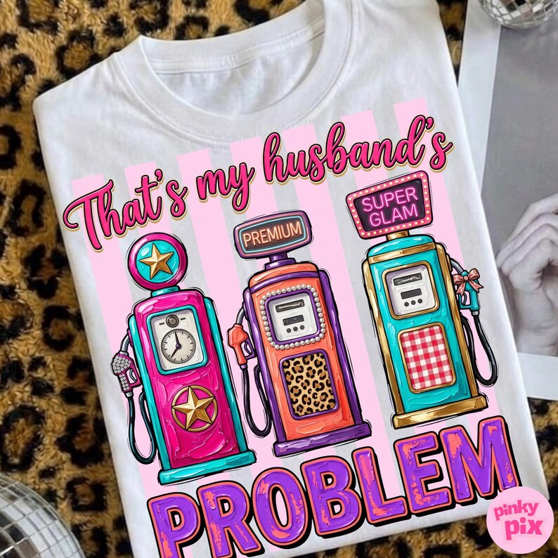 May include: White t-shirt with a graphic of three colorful gas pumps. The text on the shirt reads "That's my husband's PROBLEM" in pink and purple. The gas pumps are pink, orange, and teal.