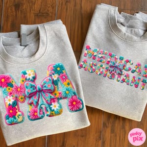 May include: Two gray sweatshirts with floral embroidered designs. One sweatshirt features the letters "MA" with a bow, and the other says "MEDICAL ASSISTANT". The embroidery includes pink, blue, yellow, and white flowers.