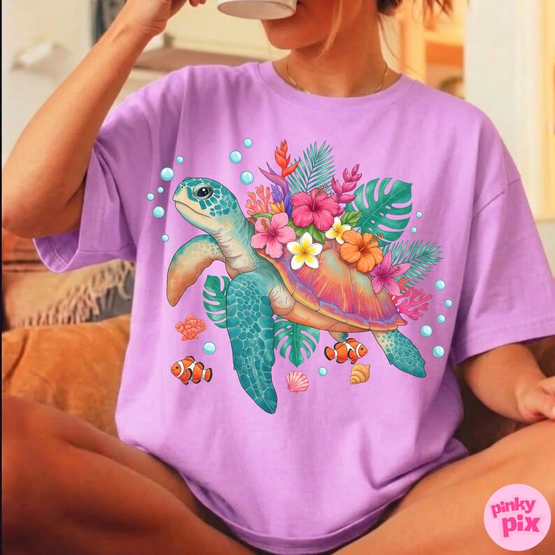 May include: A lilac-colored t-shirt featuring a colorful sea turtle design. The turtle is surrounded by tropical flowers, leaves, bubbles, and clownfish. The design has a vibrant, eye-catching aesthetic.