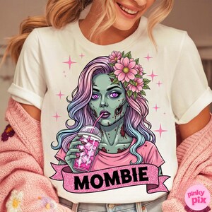May include: White t-shirt featuring a cartoon zombie woman with pink and blue hair, wearing a pink shirt and flower crown, drinking a pink beverage. The word "MOMBIE" is on a pink banner. Pink stars are in the background.