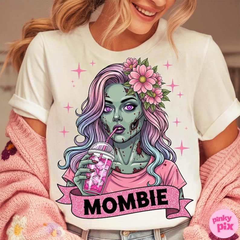May include: White t-shirt featuring a cartoon zombie woman with pink and blue hair, wearing a pink shirt and flower crown, drinking a pink beverage. The word "MOMBIE" is on a pink banner. Pink stars are in the background.