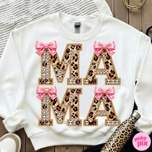 May include: White sweatshirt featuring the word "MAMA" in large, embellished letters. The letters have a leopard print pattern, are outlined in gold, and are decorated with rhinestones and pink bows. A leopard print water bottle is visible.