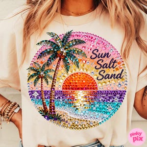 May include: Cream-colored t-shirt featuring a colorful, bejeweled graphic of a sunset over the ocean with palm trees. The words "Sun Salt Sand" are written in a script font within the design. The design is circular.