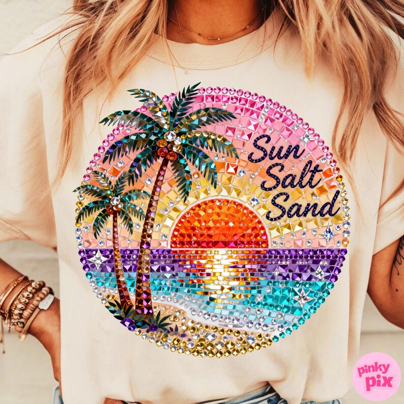 May include: Cream-colored t-shirt featuring a colorful, bejeweled graphic of a sunset over the ocean with palm trees. The words "Sun Salt Sand" are written in a script font within the design. The design is circular.