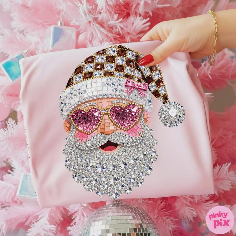 May include: A light pink fabric item featuring a decorative Santa Claus graphic composed of sparkling rhinestones. The Santa design includes a brown and white chequered hat, pink heart-shaped sunglasses, and a large, textured white crystal beard.