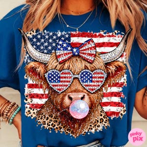 May include: Blue t-shirt featuring a cow graphic with American flag-themed sunglasses, bow, and background. The cow has a bubblegum bubble and a leopard print pattern. The Pinky Pix logo is in the bottom right corner.