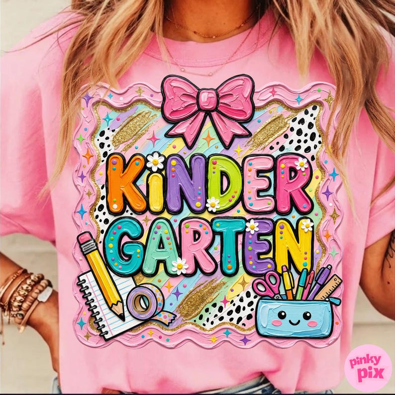 May include: Pink t-shirt with a colorful "KINDERGARTEN" graphic. The design includes a pink bow, a pencil, a notepad, and a pencil case with school supplies. The graphic is framed with a decorative border.