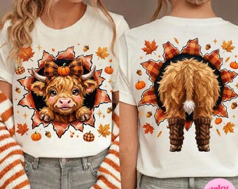 May include: A white t-shirt featuring a graphic of a fluffy Highland cow with a plaid bow on the front and the back view of the same cow wearing leg warmers. The design is framed by a torn paper effect with autumn leaves, acorns, and pumpkins.