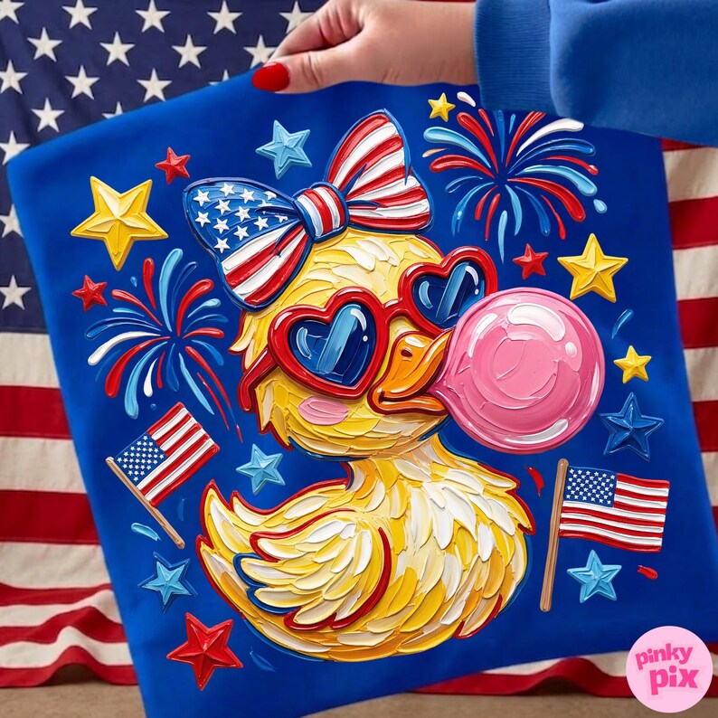May include: A blue graphic tee featuring a yellow duck wearing heart-shaped sunglasses and a bow tie, both in red, white, and blue. The duck is blowing a pink bubble, surrounded by stars, fireworks, and American flags. The design has a textured, painted look.