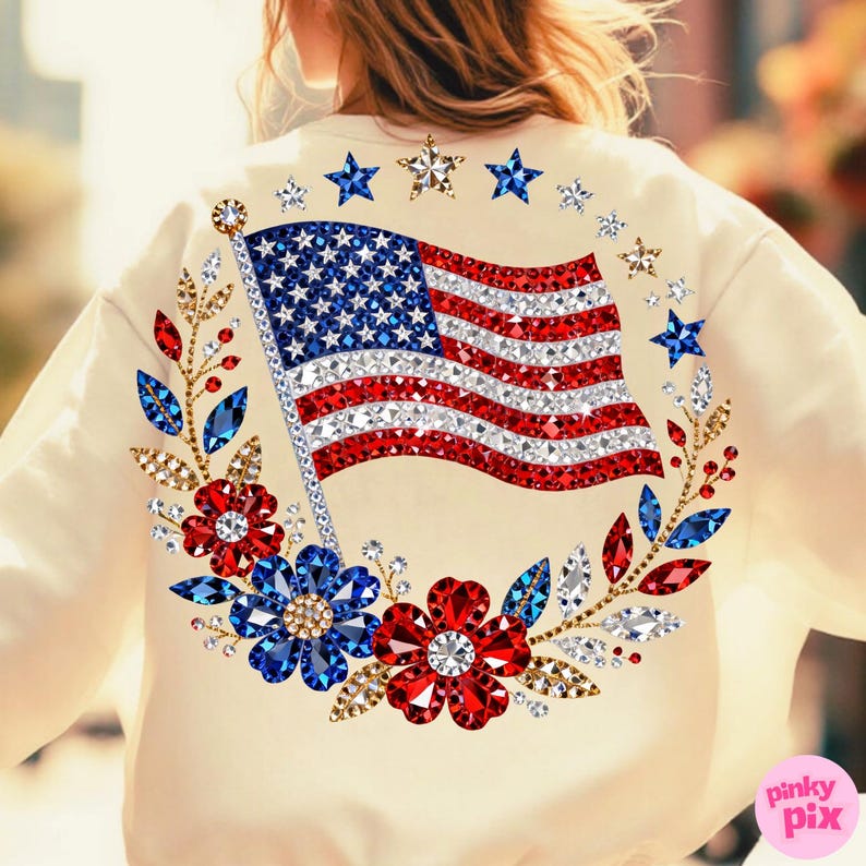 May include: Cream-colored sweatshirt featuring a sparkling American flag design. The flag is embellished with red, white, and blue rhinestones. A floral wreath with red, blue, and clear gems surrounds the flag, with star accents.