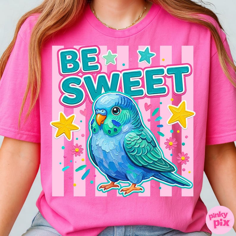May include: Pink t-shirt with a graphic of a blue parakeet and the words "BE SWEET" in turquoise. The design includes stars, flowers, and vertical stripes. The shirt is a vibrant, eye-catching piece.
