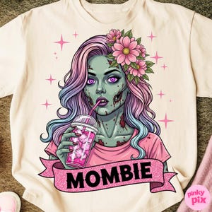 May include: Cream-colored t-shirt featuring a zombie woman with pink and blue hair, wearing a pink shirt and flower crown. She is drinking from a pink iced drink. The word "MOMBIE" is on a pink banner.