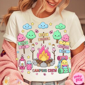May include: White t-shirt with a colorful camping-themed graphic. The design includes a campfire, trees, clouds, butterflies, and the words "Camping Crew," "Camp Fun," and "S'mores Time."