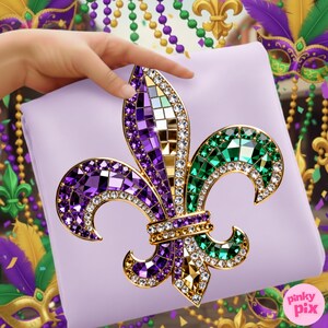 May include: A lavender fabric with a large, ornate fleur-de-lis design. The fleur-de-lis is embellished with purple, green, and gold mosaic-style gems and clear rhinestones. The design is held by a hand, with Mardi Gras-themed decorations in the background.