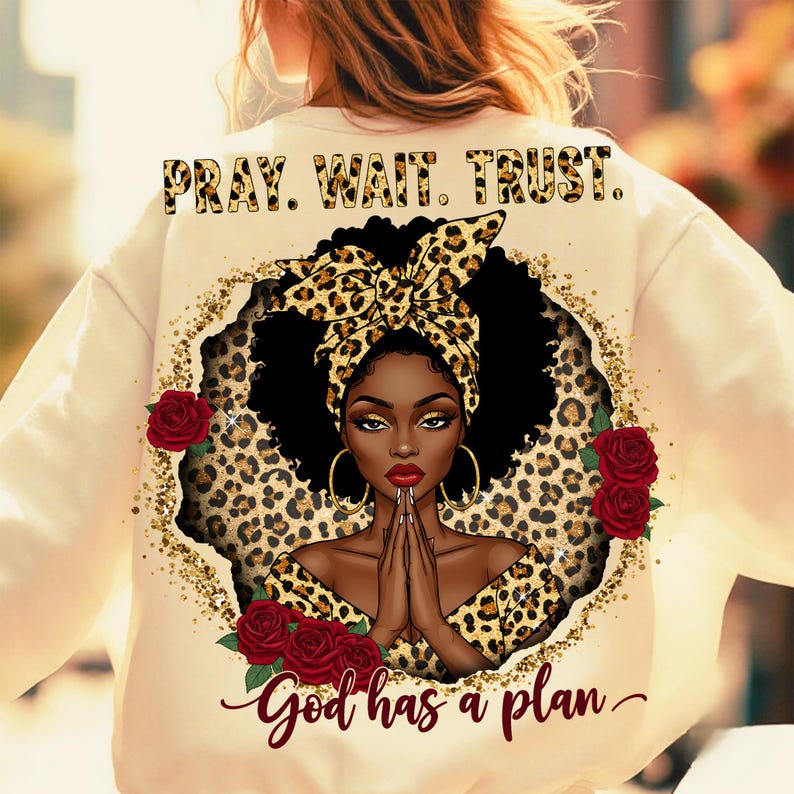 May include: A cream-colored sweatshirt with a black and gold leopard print design. The design features a woman with a leopard print headband, praying with her hands clasped together. The text "Pray. Wait. Trust. God has a plan" is printed on the sweatshirt.