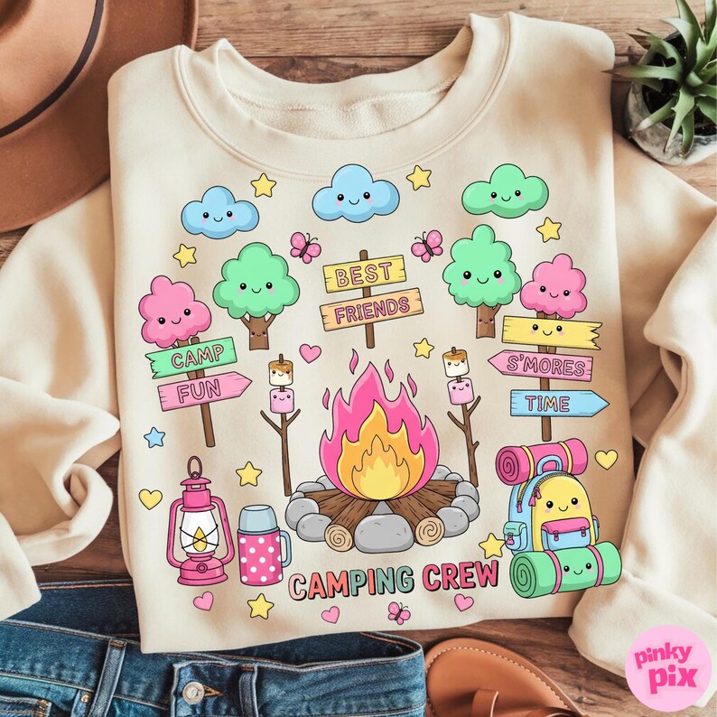 May include: Cream-colored sweatshirt with a camping-themed graphic. The design includes a campfire, trees, clouds, and the words "Camping Crew," "Best Friends," "Camp Fun," and "S'mores Time." The graphic is in a cartoon style with pastel colors.