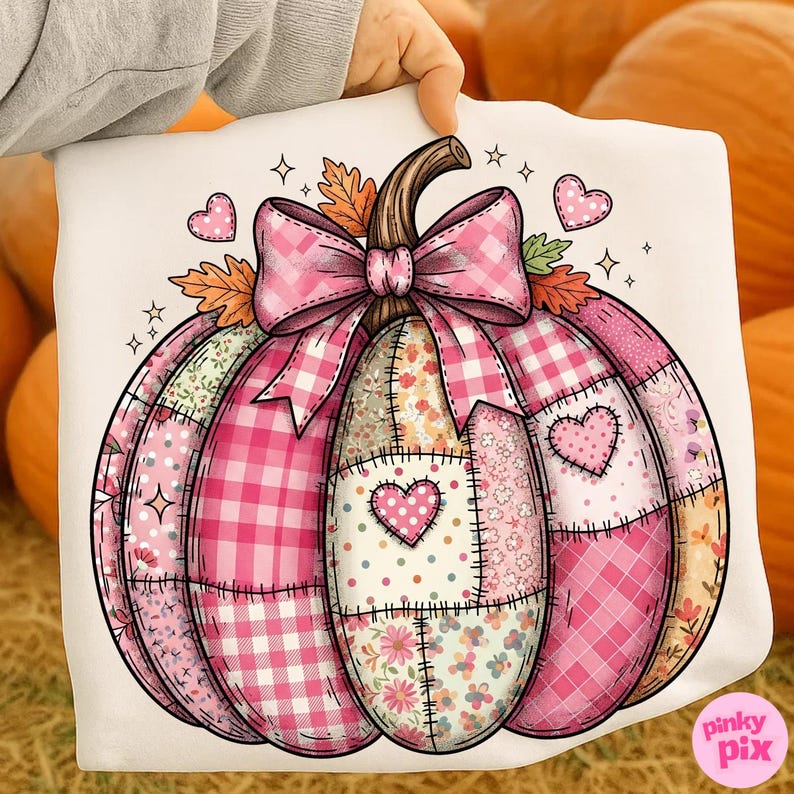 May include: A white pumpkin-shaped design with a pink bow, hearts, and autumn leaves. The pumpkin is made of various pink patterned patches, including gingham, floral, and polka dots. The design is held up by a hand.