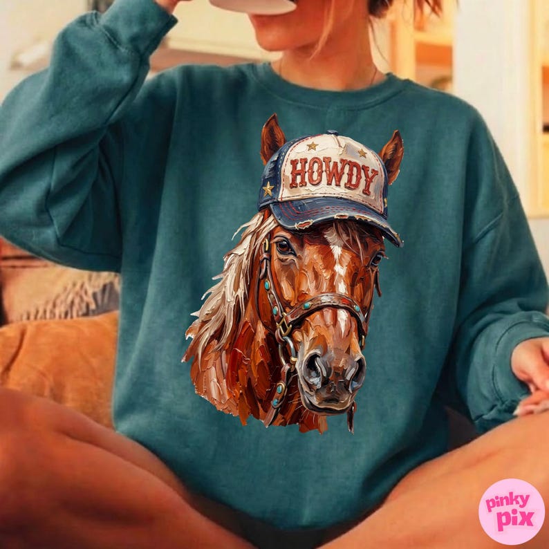 May include: Teal-colored sweatshirt featuring a detailed illustration of a horse wearing a 'HOWDY' cap. The horse has a brown coat, a white mane, and a bridle with turquoise accents. The cap is navy blue with white lettering and gold stars.