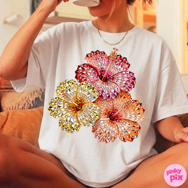 May include: White t-shirt featuring a vibrant floral design. The graphic showcases three hibiscus flowers in shades of pink, yellow, and orange, embellished with sparkling details. The shirt is a casual, everyday wear item.