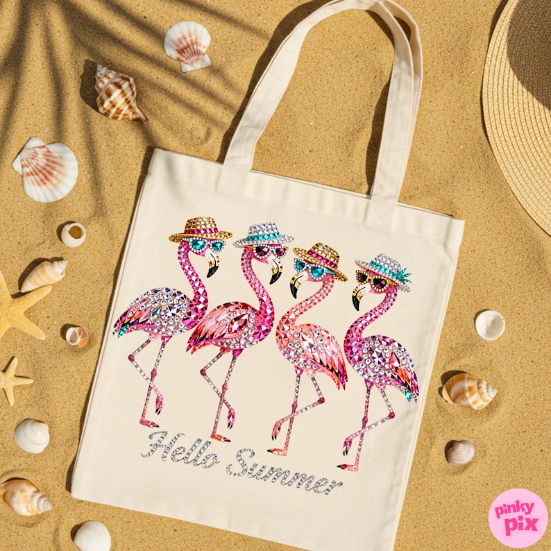 May include: Off-white canvas tote bag featuring four pink flamingo illustrations with hats and sunglasses. The flamingos are embellished with rhinestones. The words "Hello Summer" are written in silver glitter. Seashells and a straw hat are in the background.