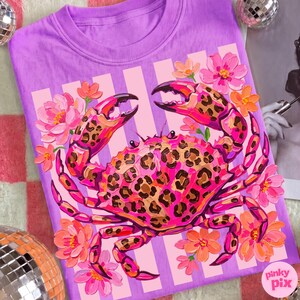May include: A lilac-colored t-shirt featuring a vibrant crab design. The crab has a leopard print pattern in shades of pink and brown, surrounded by pink and orange flowers. The shirt has vertical white stripes and the text "pinky pix".