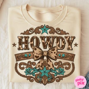 Pu&ograve; includere: Una felpa color crema con un designo marrone, bianco e turchese. Il design presenta un grande "HOWDY" con un motivo a pelle di mucca, una stella turchese e un fiocco marrone con un motivo a pelle di mucca. Il design &egrave; circondato da volute marroni ornate.