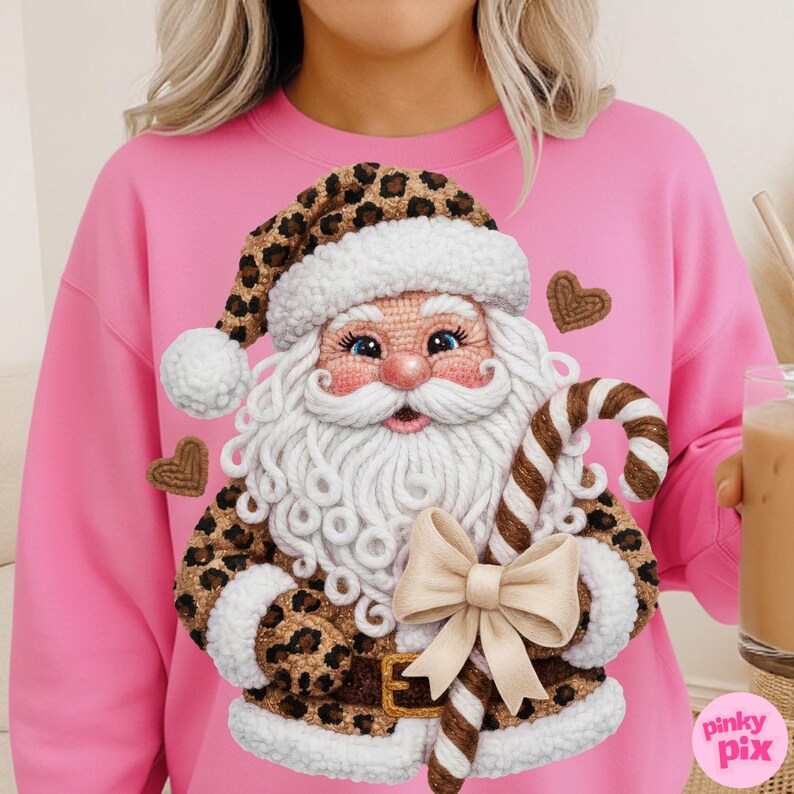May include: Pink sweatshirt featuring a detailed Santa Claus design with a leopard print hat and coat trim. Santa holds a candy cane and a bow. The design includes heart-shaped accents. The sweatshirt has a crew neck.