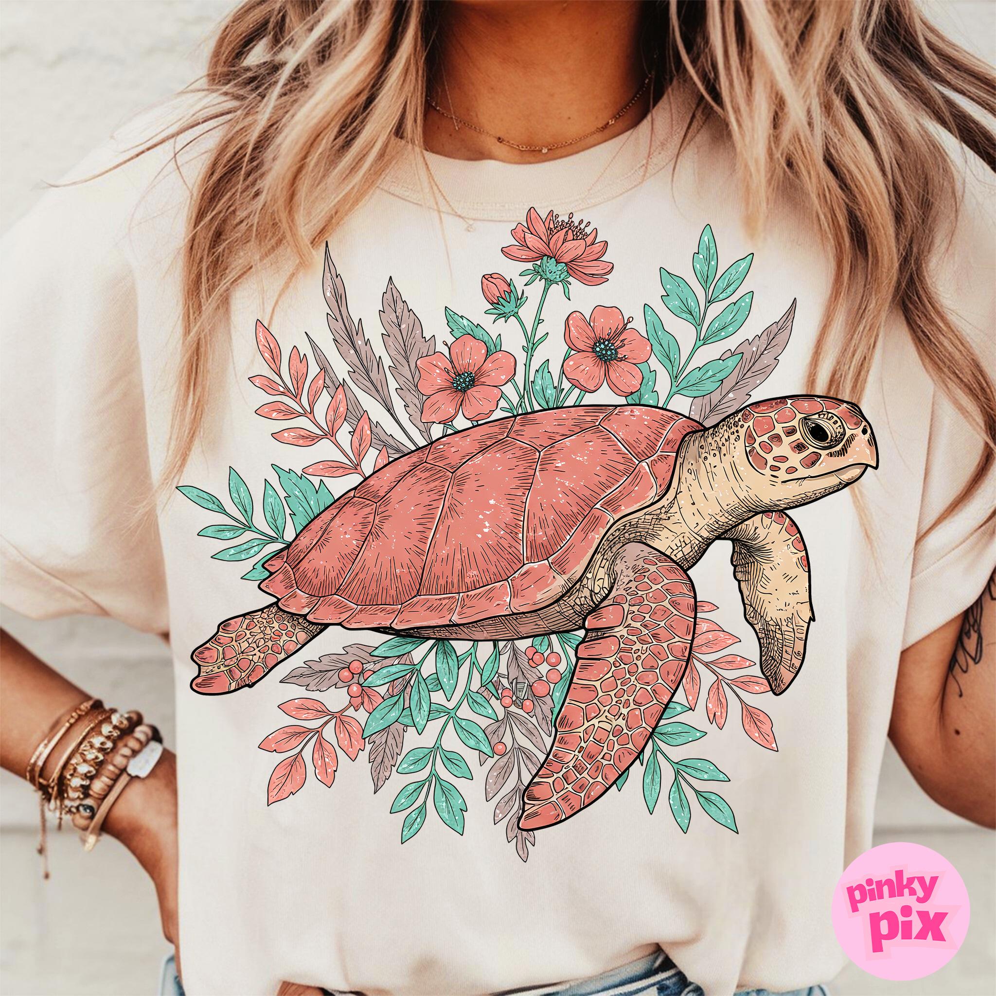 May include: A white t-shirt with a pink and green floral design featuring a sea turtle. The turtle is outlined in black and has a detailed shell.