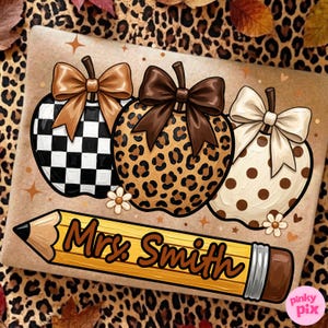May include: A tan fabric surface featuring a graphic of three pumpkins with bows, one with a black and white checkerboard pattern, one with a leopard print, and one with brown polka dots, plus a yellow pencil with the text Mrs. Smith.