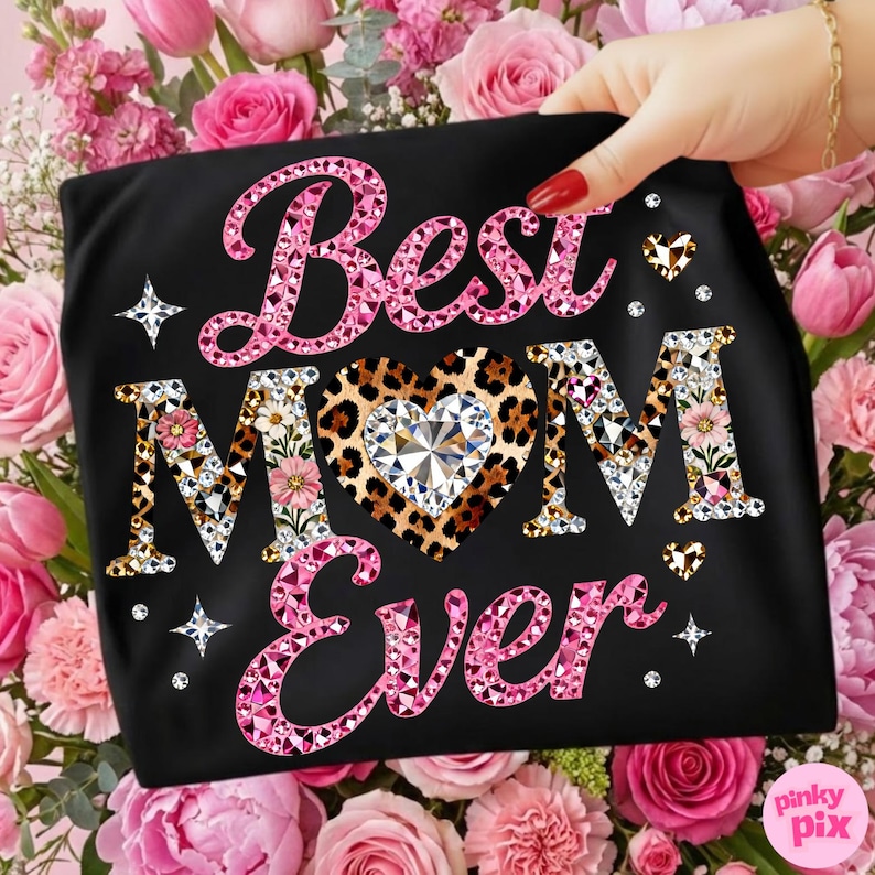 May include: Black t-shirt with the text "Best MOM Ever" in pink, leopard print, and rhinestone lettering. The design includes a leopard print heart with a large crystal in the center, surrounded by pink flowers and diamonds. The shirt is held in front of a background of pink roses.