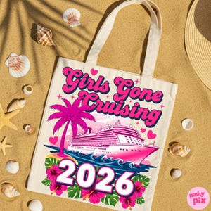 May include: A cream-colored tote bag with the text "Girls Gone Cruising 2026" in pink and blue. The design includes a pink cruise ship, palm tree, and hibiscus flowers. The bag is on a sandy surface with seashells.