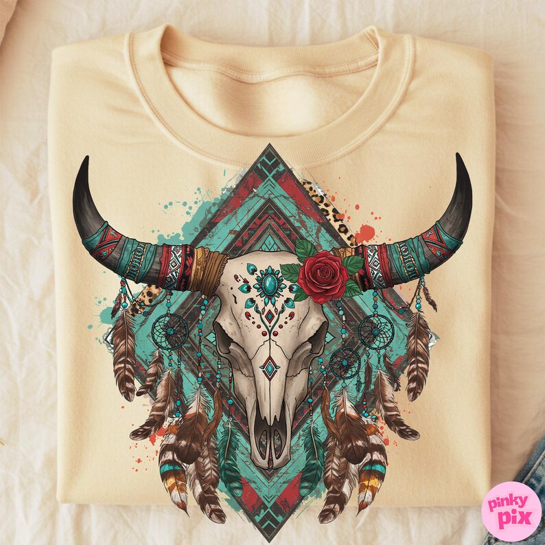 May include: Cream-coloured sweatshirt with a detailed graphic of a bull skull adorned with turquoise, red, and brown tribal patterns. The design includes a red rose, feathers, and dream catchers, creating a bohemian aesthetic.