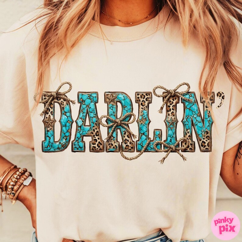 Pu&ograve; includere: T-shirt beige chiaro con la scritta "DARLIN'" in turchese, stampa leopardata e dettagli in corda marrone. Le lettere sono riempite con un motivo a pietra turchese, per uno stile western.