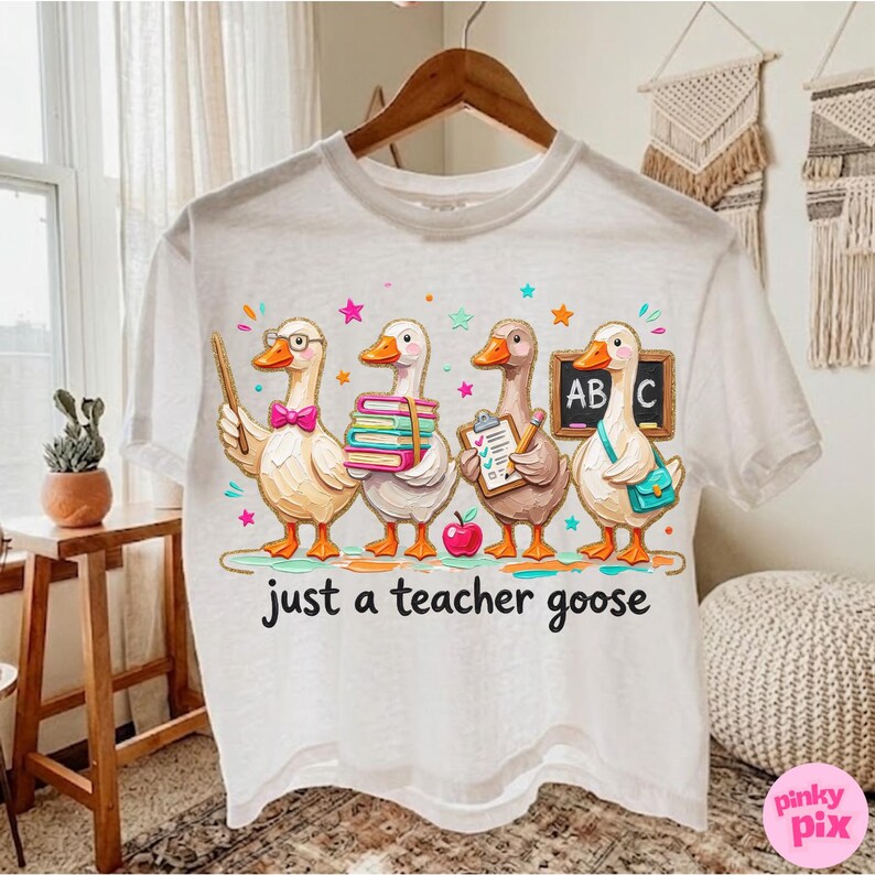 May include: White t-shirt featuring a whimsical illustration of four cartoon geese dressed as teachers. The geese are holding books, a clipboard, and a pointer. The text "just a teacher goose" is printed below the geese.