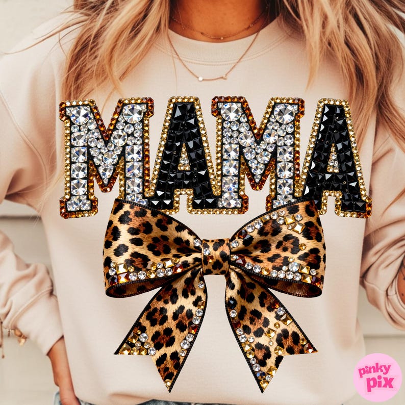 Pu&ograve; includere: Una felpa beige con la scritta "MAMA" in grandi lettere gioiello. Le lettere sono bordate d'oro e riempite di gemme chiare e nere. Un fiocco leopardato con accenti di gemme &egrave; sotto la scritta.