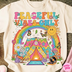 May include: Cream-colored t-shirt with a colorful graphic design. The design features the text "PEACEFUL VIBES ONLY" above a rainbow, butterflies, a smiling sun, and a tent. Additional elements include flowers, mushrooms, and a record player.