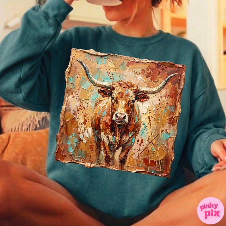 May include: Teal-colored sweatshirt featuring a detailed painting of a longhorn steer. The artwork showcases the steer's head and horns, with a textured, abstract background in shades of brown, tan, and turquoise. The sweatshirt is a comfortable, casual style.