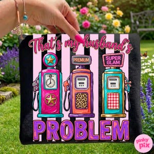 May include: Black tote bag with a graphic of three colorful vintage gas pumps. The text "That's my husband's PROBLEM" is above the pumps in pink and purple. The pumps are pink, orange, and teal with star and leopard print details.