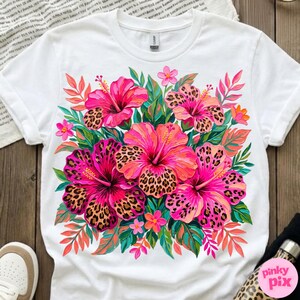 May include: White t-shirt featuring a vibrant floral design. The design showcases pink hibiscus flowers with leopard print centers, surrounded by green leaves and smaller pink flowers. The shirt has a classic crew neck and short sleeves.