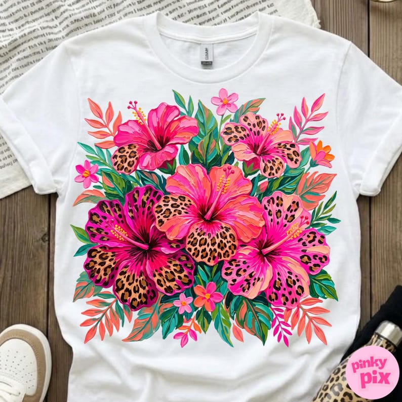 May include: White t-shirt featuring a vibrant floral design. The design showcases pink hibiscus flowers with leopard print centers, surrounded by green leaves and smaller pink flowers. The shirt has a classic crew neck and short sleeves.