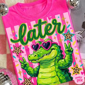 May include: A bright pink t-shirt featuring a green alligator wearing heart-shaped sunglasses and giving a peace sign. The word "later" is written in green script above the alligator. The design includes stars and stripes.