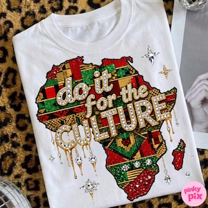 Peut inclure: T-shirt blanc avec une carte de l'Afrique ornée de motifs rouges, verts et dorés. Le texte "do it for the CULTURE" est en or et cristaux. Des détails en cristal ornent le design.