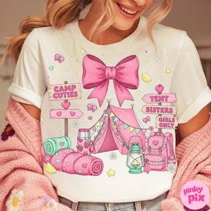 May include: White t-shirt featuring a pink bow and camping graphics. The design includes a pink tent, a backpack, a lantern, and the text "Camp Cuties" and "Tent Sisters Girls Only". The shirt has a whimsical, cute style.